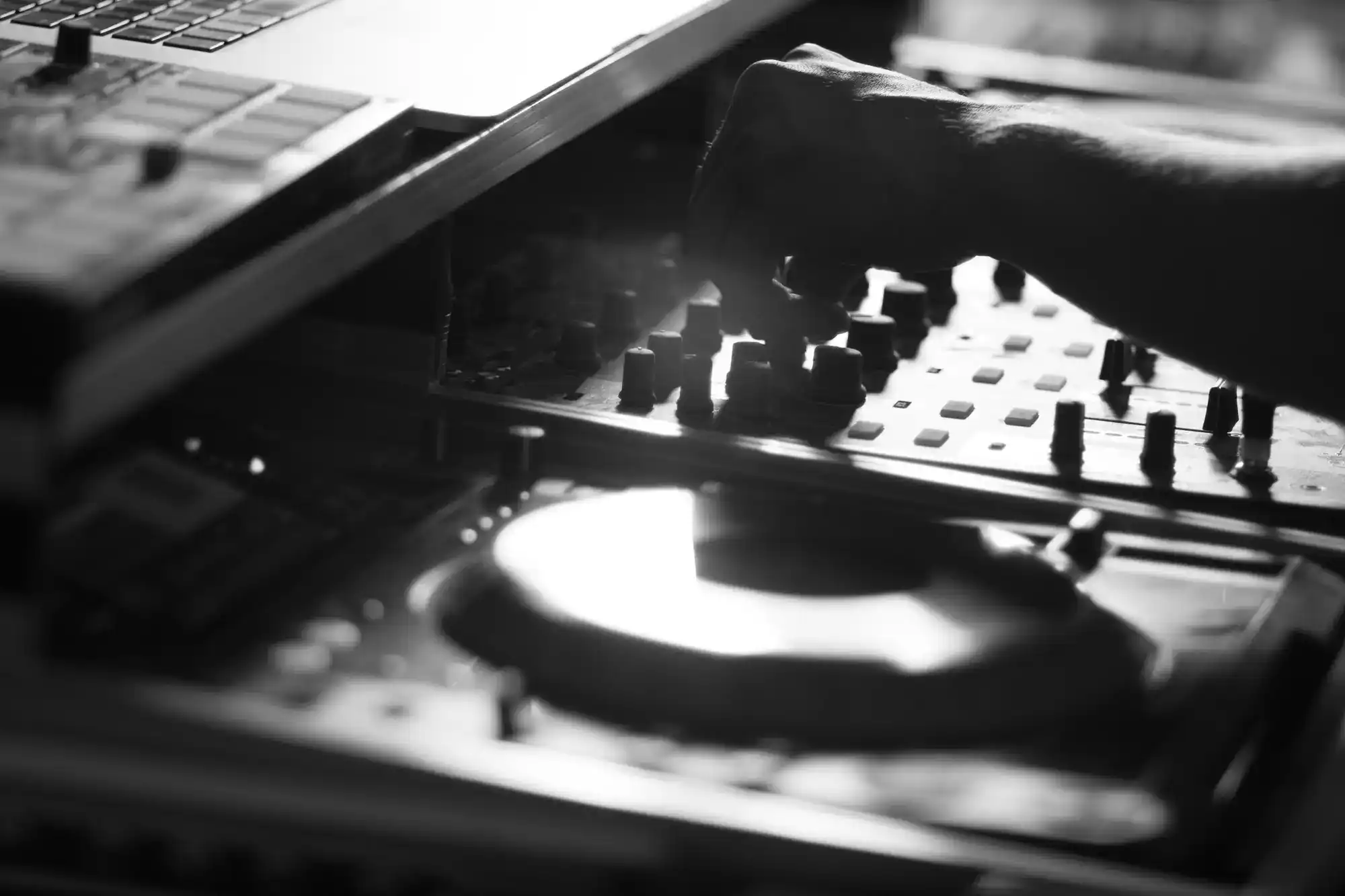 A wedding DJ in Minnesota and Wisconsin adjusts a mixing console next to a laptop, shown in black and white.