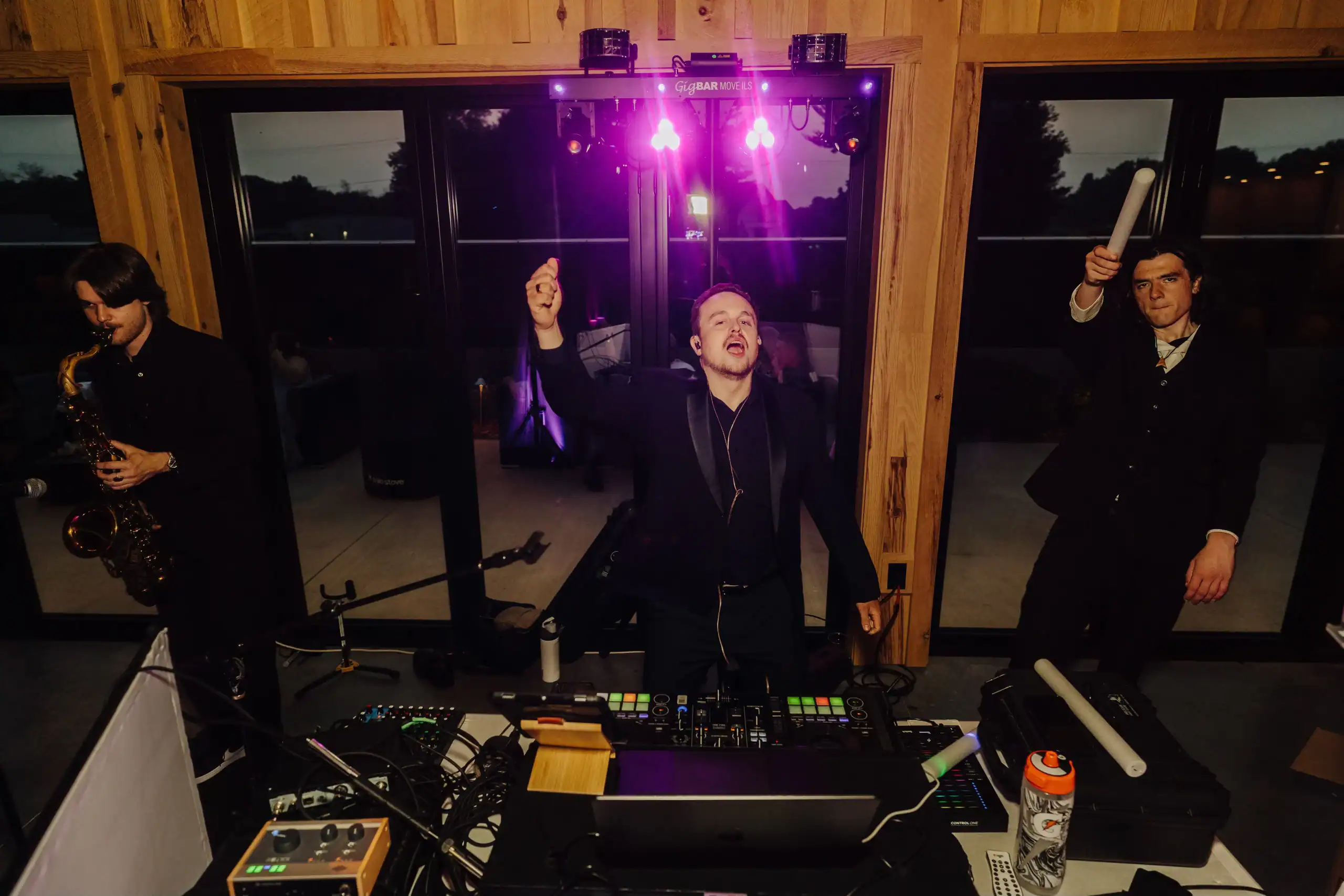 Three musicians play indoors at night with DJ gear from a top wedding entertainment company in Minnesota.
