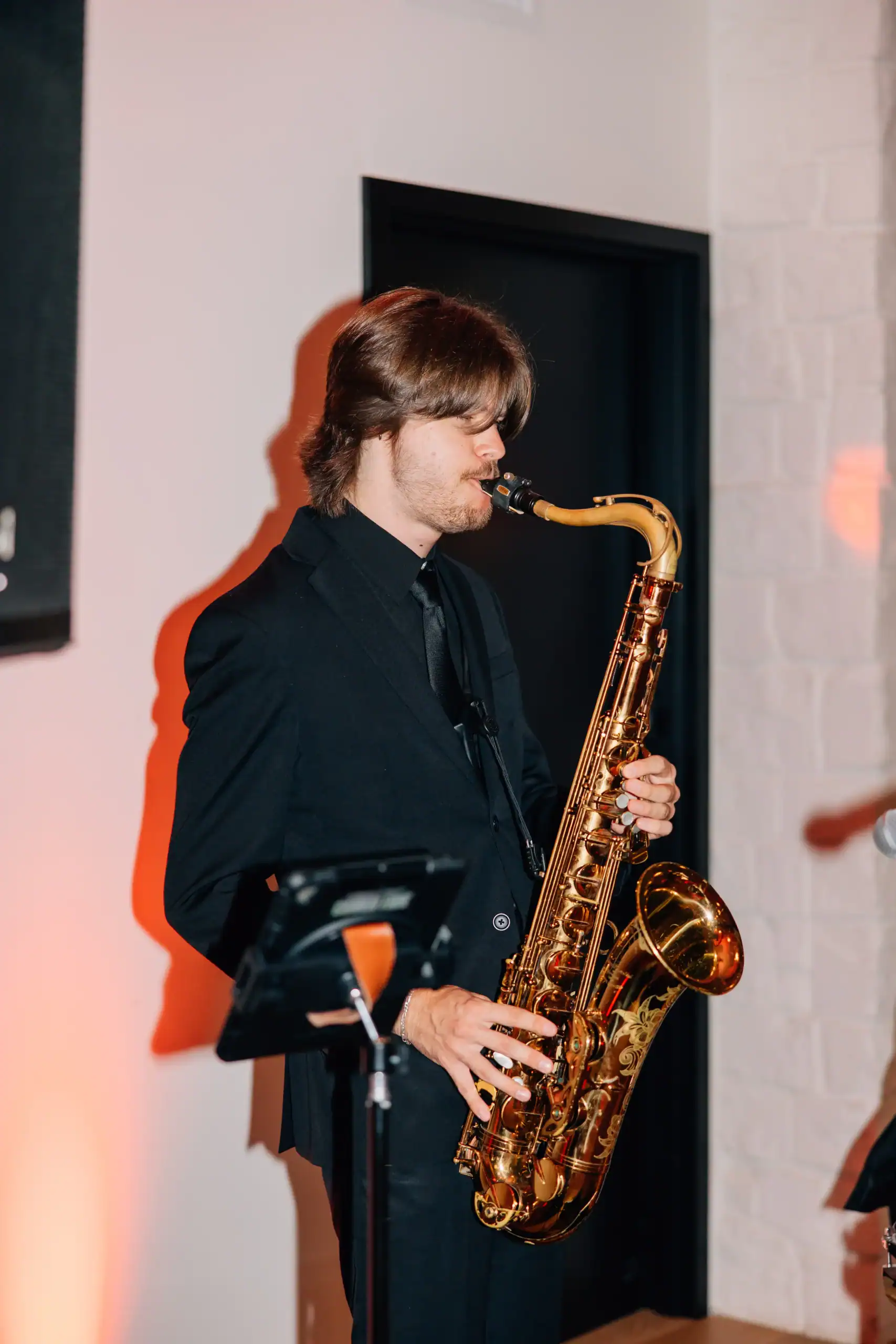 A man in a black suit from a Minnesota and Wisconsin wedding entertainment company plays saxophone indoors.